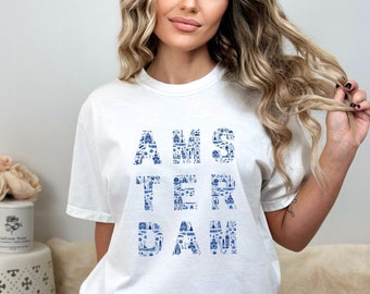 May include: White t-shirt with a blue graphic design of the word "AMSTERDAM" made up of small images of Amsterdam landmarks.