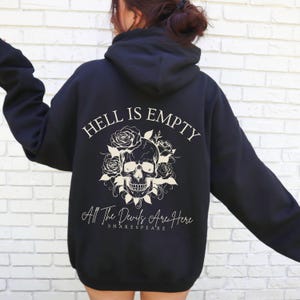 Puede incluir: Sudadera con capucha negra con un diseño de calavera blanca y flores en la espalda. El texto "Hell is Empty All The Devils Are Here Shakespeare" está impreso debajo del diseño.