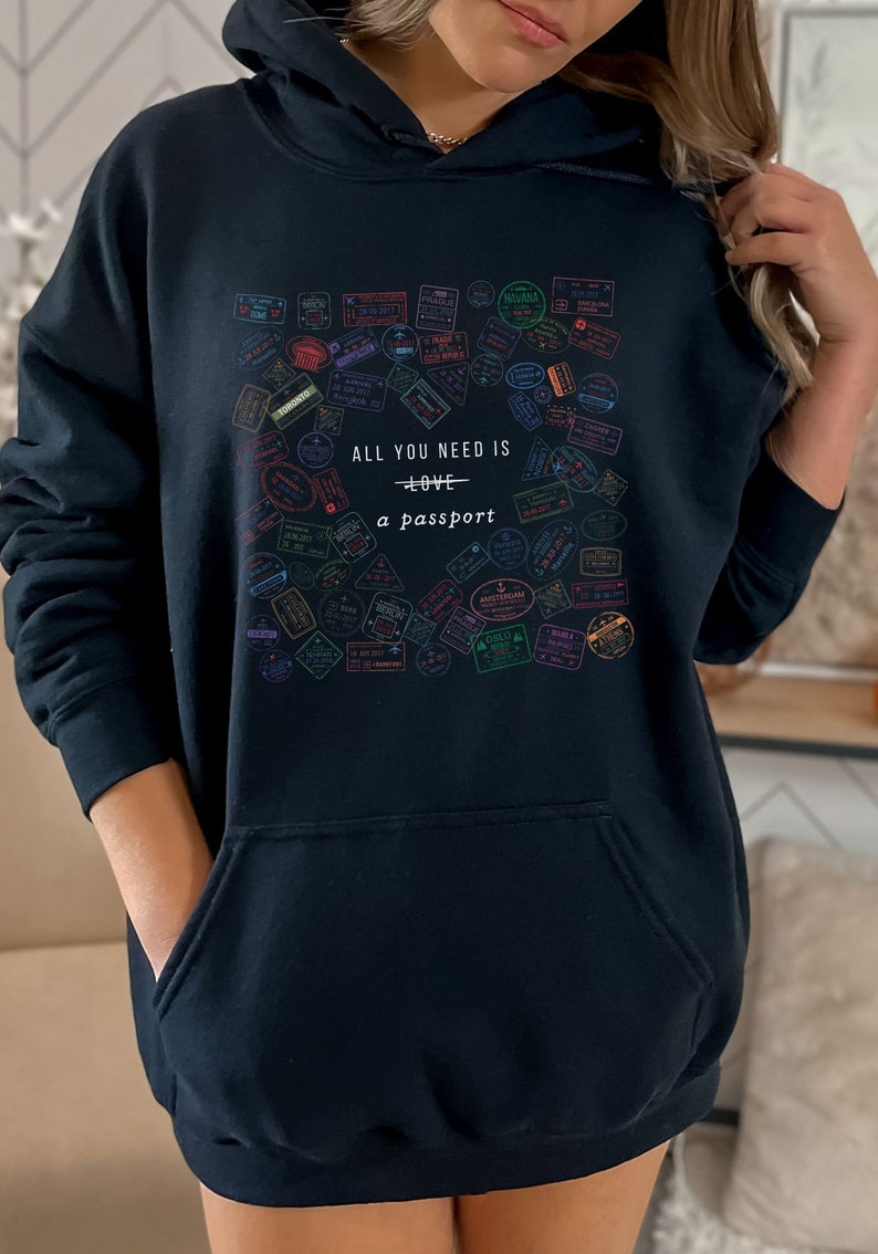 May include: Black hooded sweatshirt with a graphic print of colorful passport stamps and the text "All you need is love + a passport".