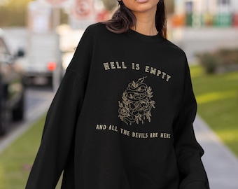 Op de afbeelding: Zwart sweatshirt met een gouden grafische print van een slang en bloemen. De tekst "De hel is leeg en alle duivels zijn hier" staat op het sweatshirt gedrukt.