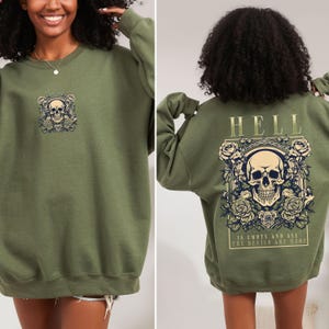 Puede incluir: Una sudadera verde con un gráfico de calavera y rosas en la parte delantera y el texto "HELL IS EMPTY AND ALL THE DEVILS ARE HERE" en la parte trasera.