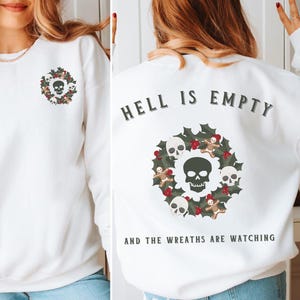Puede incluir: Sudadera blanca con un diseño de calavera y corona en la parte delantera y el texto "El infierno está vacío y las coronas están mirando" en la parte trasera.