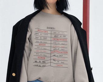 May include: A grey sweatshirt with a graphic print of a list of dates and words, including "Helping", "Introverts", "Avoid", "Conversation", and "Since".