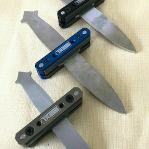 Puede incluir: Tres herramientas de afilado de cuchillos con mangos de diferentes colores. Las herramientas están fabricadas por TR Maker y están diseñadas para afilar cuchillos.