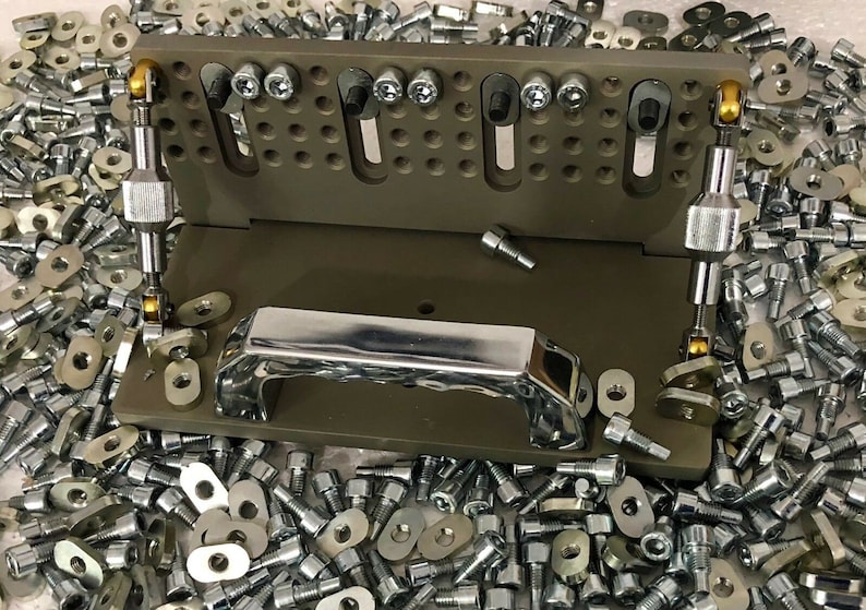 May include: A brown metal tool with a chrome handle and two adjustable arms. The tool is surrounded by a large quantity of screws and washers.
