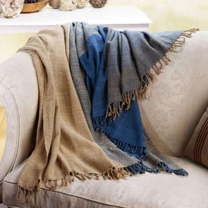 Peut inclure: Une couverture en laine de couleur marron et bleu avec des franges sur les bords, posée sur un canapé. La couverture est faite d'un tissu doux et texturé.