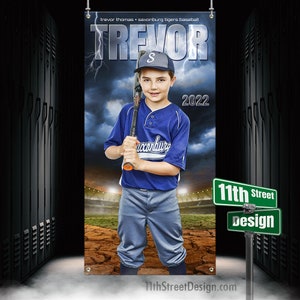 May include: A baseball banner featuring a young boy in a blue and white uniform, holding a bat. The banner has the name "TREVOR" in large letters, with "2022" below. The background shows a stormy sky and a baseball field.