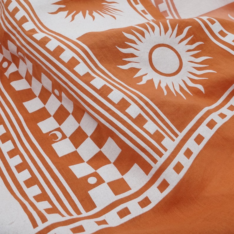 Puede incluir: Tela naranja con un patr&oacute;n geom&eacute;trico blanco con soles y lunas. El patr&oacute;n incluye un dise&ntilde;o de tablero de ajedrez y un borde repetitivo.