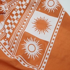 Puede incluir: Tela naranja con un patr&oacute;n de cuadros blancos y dise&ntilde;os de sol blancos. La tela tiene un borde blanco con un patr&oacute;n repetitivo.