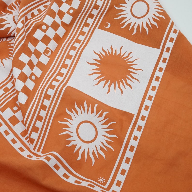 Puede incluir: Tela naranja con un patr&oacute;n de cuadros blancos y dise&ntilde;os de sol blancos. La tela tiene un borde blanco con un patr&oacute;n repetitivo.