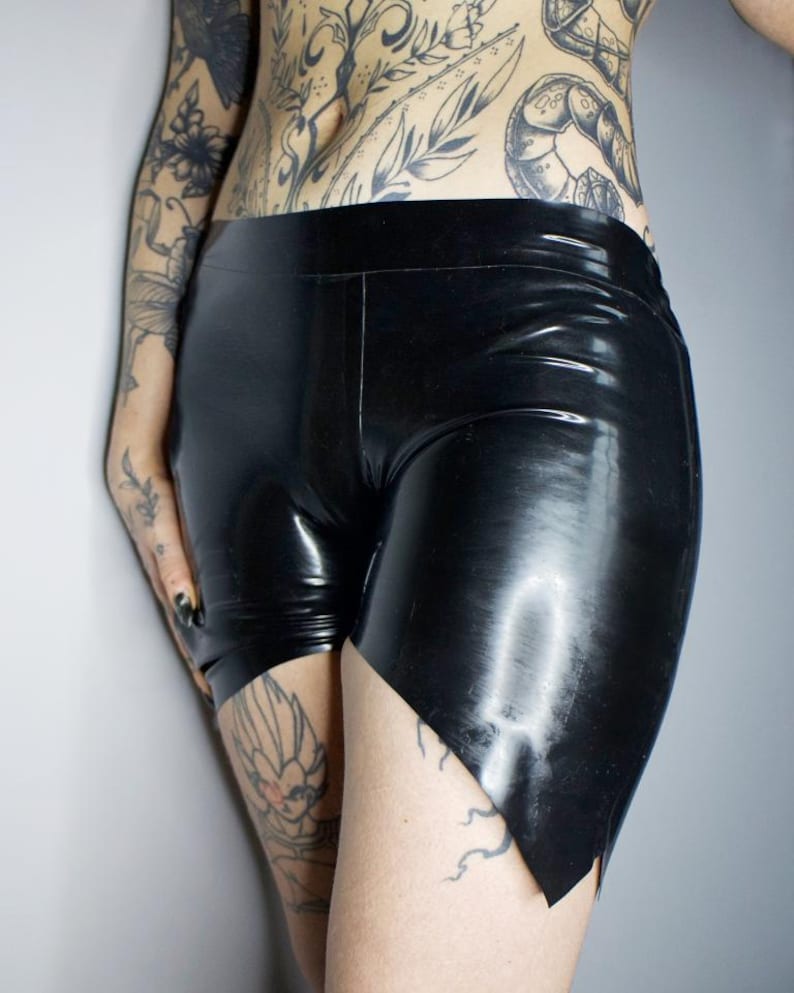 May include: Black latex shorts with a high waist and a unique asymmetrical hemline. The shorts have a glossy finish and a form-fitting design. The shorts are made of a shiny, smooth material.