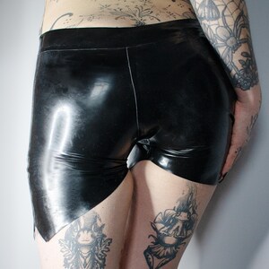 May include: Black latex shorts with a high waist and a glossy finish. The shorts have a unique cut on the leg openings. The image shows the shorts from the back and side.