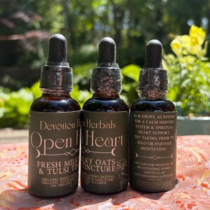 K&ouml;nnte beinhalten: Drei braune Glasflaschen mit schwarzen Tropfkappen. Die Flaschen haben Etiketten mit dem Text "Devotion Herbals" und "Open Heart". Die Etiketten listen auch Inhaltsstoffe und Gebrauchsanweisungen auf. Die Flaschen stehen auf einer gemusterten Oberfl&auml;che.