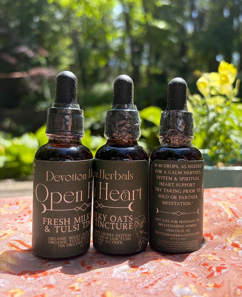 K&ouml;nnte beinhalten: Drei braune Glasflaschen mit schwarzen Tropfkappen. Die Flaschen haben Etiketten mit dem Text "Devotion Herbals" und "Open Heart". Die Etiketten listen auch Inhaltsstoffe und Gebrauchsanweisungen auf. Die Flaschen stehen auf einer gemusterten Oberfl&auml;che.