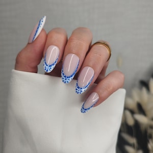May include: Oval-shaped artificial nails with a nude base and a blue floral design along the edges. The nails are painted with a thin blue line and small blue floral accents. The design is visible on multiple nails.