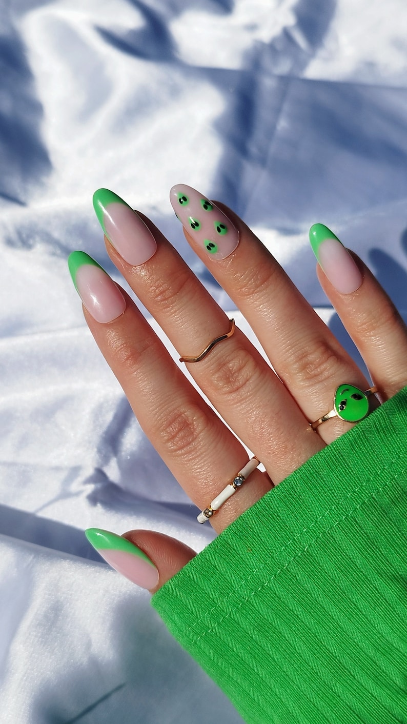 May include: Green and pink ombre nail tips with a black alien face design.
