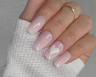 May include: Pink coffin-shaped press-on nails with a white heart design on one nail.