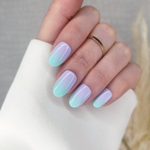 Peut inclure: Gros plan sur une main avec cinq ongles ovales peints avec un dégradé de bleu clair à violet.