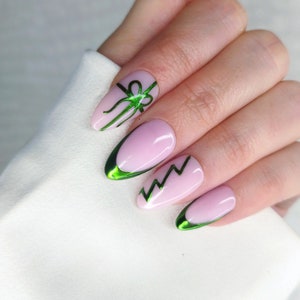 May include: Pink oval-shaped nails with green glitter accents. The nails feature a green bow design on one nail and a green lightning bolt design on another nail.