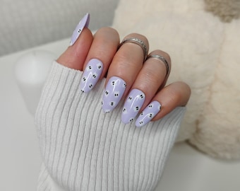 May include: A set of lavender-colored press-on nails with a white and black cloud design.