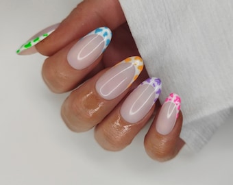 May include: Oval-shaped, long artificial nails with a French manicure design. The tips are decorated with colourful, irregular patterns in blue, orange, purple, and pink. One nail has a green tip. The nails are on a hand.