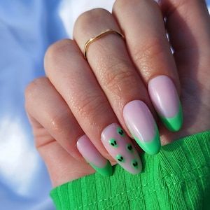 May include: Close-up of a hand with light pink oval-shaped nails with a green tip and black alien face designs.