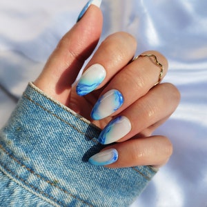 May include: Close-up of a hand with blue and white marble nail polish. The nails are long and oval shaped. The hand is wearing a gold ring.