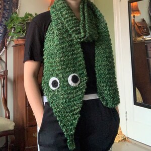 Puede incluir: Una bufanda de punto verde con ojos saltones. La bufanda es larga y tiene un patr&oacute;n de punto texturizado.
