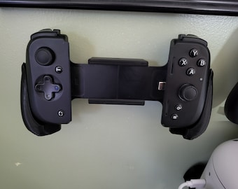 May include: A black gaming controller with a phone holder in the middle. The controller has buttons labeled A, B, X, Y, and a directional pad. The phone holder is made of black plastic.
