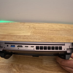 May include: A dark gray laptop with a black rubberized grip on each side. The laptop has a USB port, HDMI port, and a power port on the side. The laptop is sitting on a wooden surface.