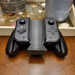 May include: A black Nintendo Switch controller with two detachable grips. The controller has a textured surface and features buttons labeled "Start" and "Select".