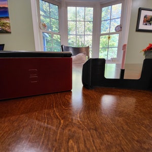 May include: A red Nintendo DS game console with a black screen and a black stand. The console is closed and the stand is open.