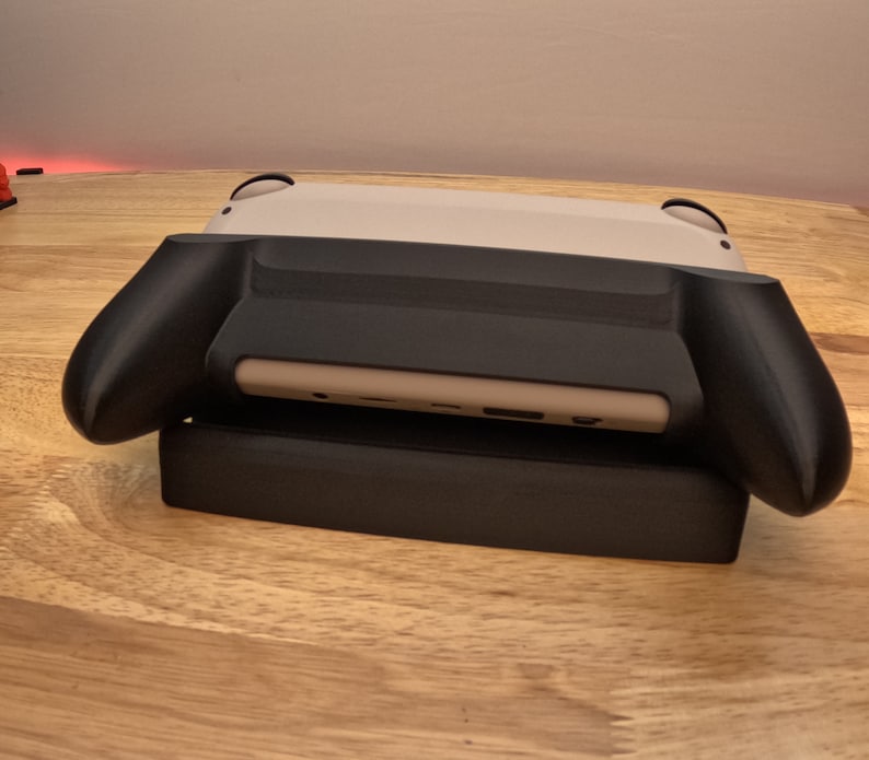 K&ouml;nnte beinhalten: Eine wei&szlig;e und schwarze Nintendo Switch-Konsole mit einer schwarzen Schutzh&uuml;lle. Die Konsole liegt auf einer Holzoberfl&auml;che.