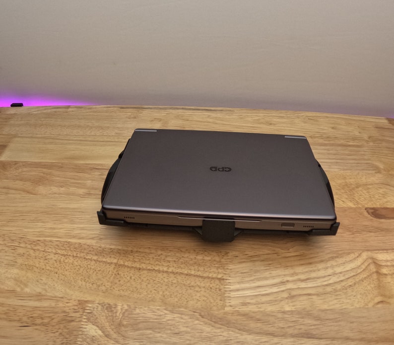 May include: A closed, dark gray laptop computer with a black plastic laptop stand. The laptop is sitting on a light wood surface.