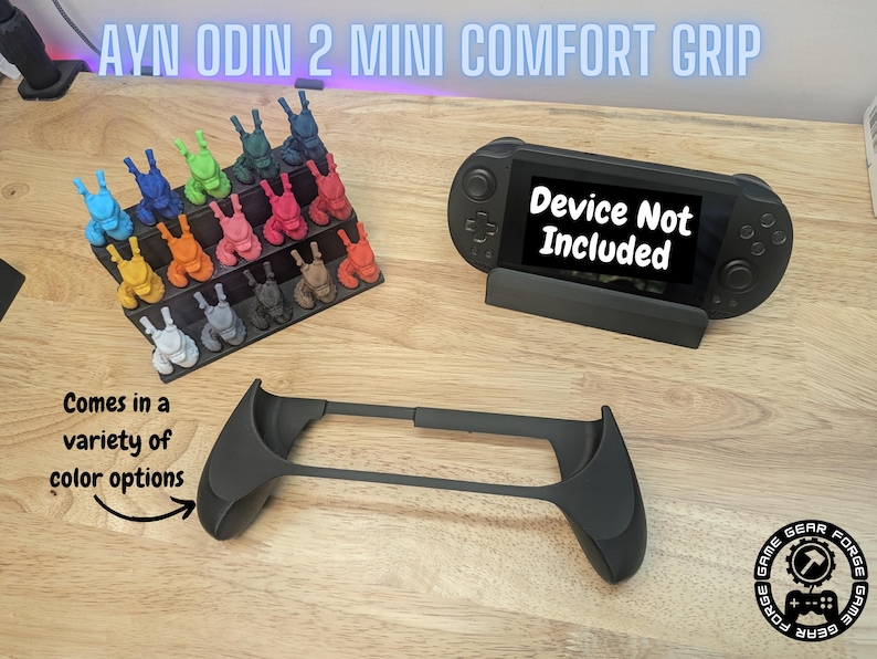 Puede incluir: Una empu&ntilde;adura de confort negra impresa en 3D para el dispositivo de juego port&aacute;til AYN Odin 2 Mini. La empu&ntilde;adura est&aacute; dise&ntilde;ada para mejorar la comodidad y el control durante el juego. La imagen tambi&eacute;n muestra una variedad de opciones de color para la empu&ntilde;adura. El texto "Dispositivo no incluido" se muestra en el dispositivo port&aacute;til.