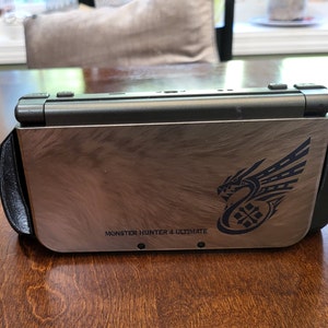 May include: A black Nintendo Switch console with a custom Monster Hunter 4 Ultimate design. The console has a black dragon design with a gold background.