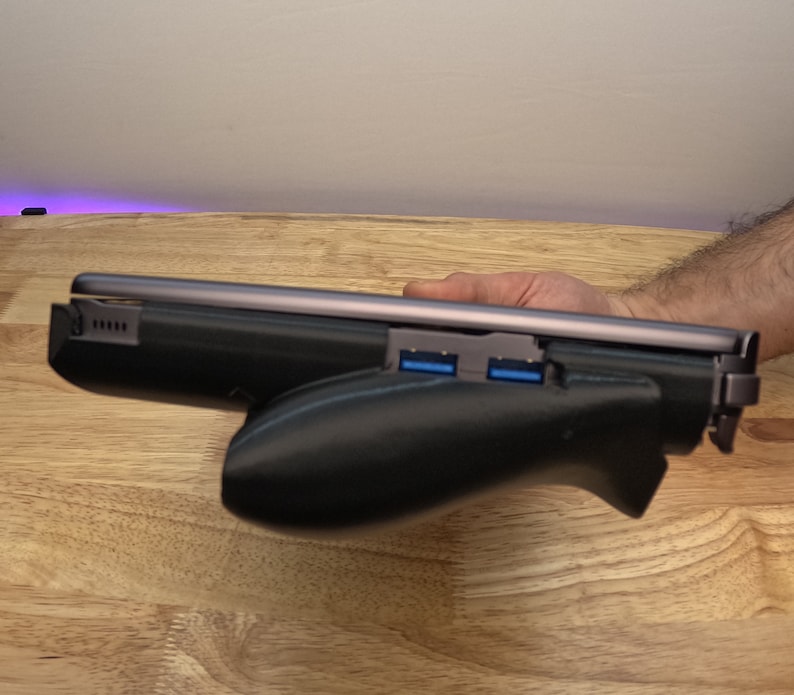 May include: A black laptop with a built-in handle and two blue USB ports. The laptop is closed and lying on a wooden surface.
