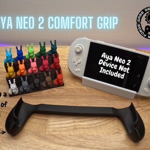 May include: Black plastic grip for the Aya Neo 2 handheld gaming device. The grip is designed to provide a more comfortable hold. The text "Aya Neo 2 Device Not Included" is displayed on a white handheld gaming device.