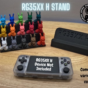 Op de afbeelding: Een zwarte standaard voor het handheld gaming-apparaat RG35XX H. De standaard is gelabeld "RG35XX H". De standaard wordt getoond met een verscheidenheid aan gekleurde beeldjes. De tekst "RG35XX H Device Not Included" staat op een handheld gaming-apparaat.