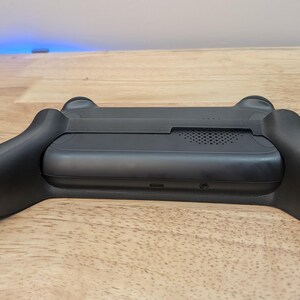 Puede incluir: Consola de juegos port&aacute;til negra con agarre texturizado y altavoz integrado. La consola tiene un puerto USB-C y una toma de auriculares.