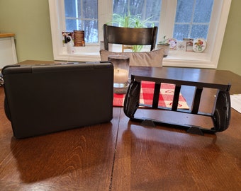 May include: A black laptop computer closed and a black plastic stand for a laptop computer on a wooden table.
