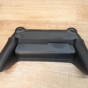 Puede incluir: Controlador de juegos port&aacute;til negro con agarres texturizados y un ventilador incorporado para enfriamiento. El controlador tiene una correa para mayor seguridad.