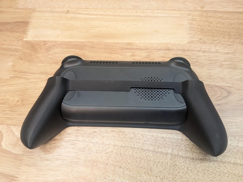 Puede incluir: Controlador de juegos port&aacute;til negro con agarres texturizados y un ventilador incorporado para enfriamiento. El controlador tiene una correa para mayor seguridad.