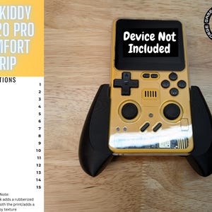 以下が含まれることがあります： 黒いコントローラーグリップが付いた金色の携帯ゲーム機。デバイスには、「Device Not Included」というテキストが表示された黒い画面があります。デバイスは木製の表面に置かれています。画像には、デバイスのカラーオプションのリストも含まれており、各カラーの横に番号が付けられています。