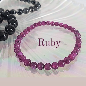 May include: A red ruby gemstone bracelet with round beads. The bracelet is on a white background with the word "Ruby" written in black.