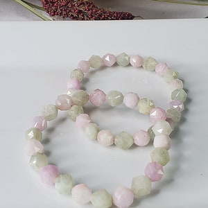 May include: A bracelet made of light green and pink faceted gemstone beads. The beads are arranged in a repeating pattern of light green and pink.