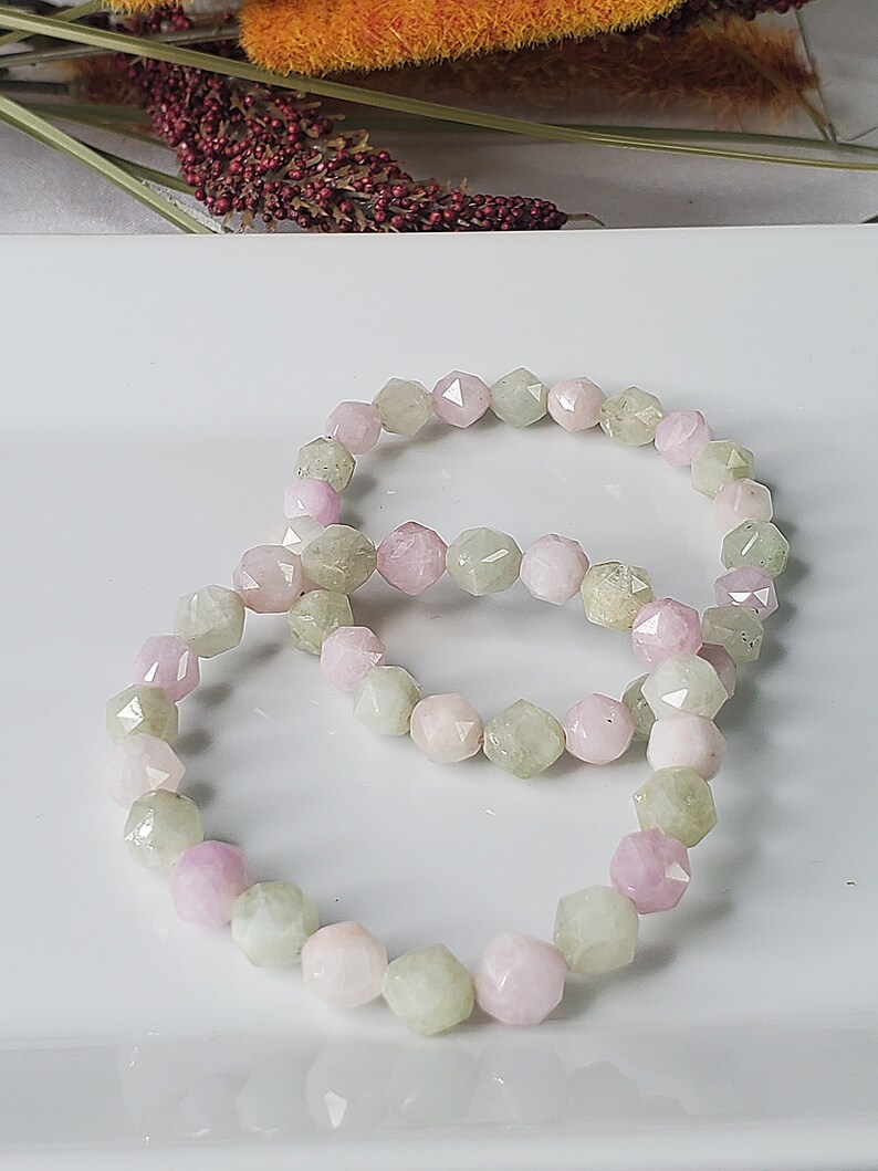 May include: A bracelet made of light green and pink faceted gemstone beads. The beads are arranged in a repeating pattern of light green and pink.