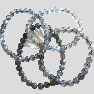 May include: Three gray labradorite gemstone bracelets with iridescent blue and green hues. The bracelets are made of round beads and are stacked on top of each other.