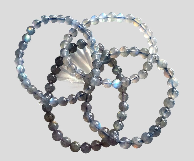May include: Three gray labradorite gemstone bracelets with iridescent blue and green hues. The bracelets are made of round beads and are stacked on top of each other.