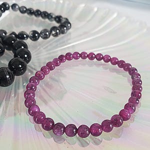 May include: A pink gemstone bracelet with round beads. The bracelet is made of small, round beads that are strung together on a clear elastic cord.